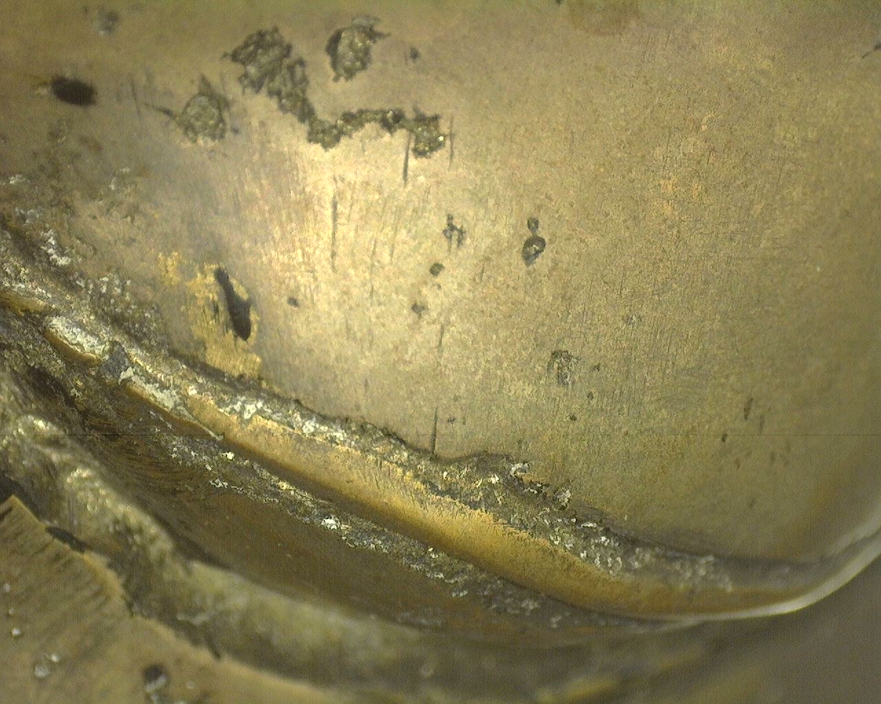 Forensische macro-opname van de messing-bronzen giethuid met legitieme wit-grijze kristallijne afzettingen in de diepe montageranden.