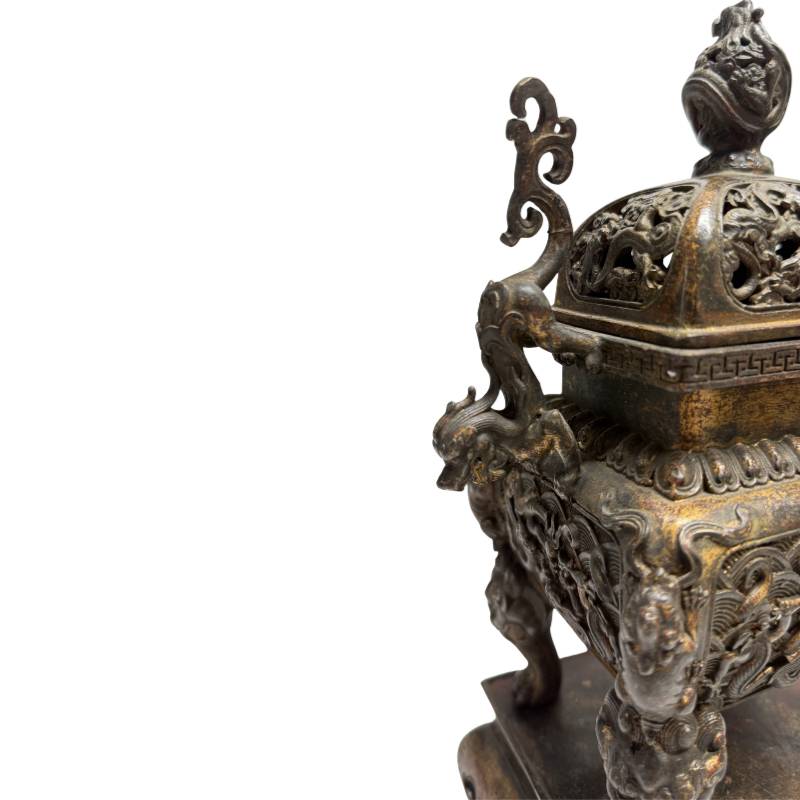 Sfeervolle detailopname van het linker handvat in de vorm van een klimmende draak en het diepe reliëf op de hoek van de bronzen brander.