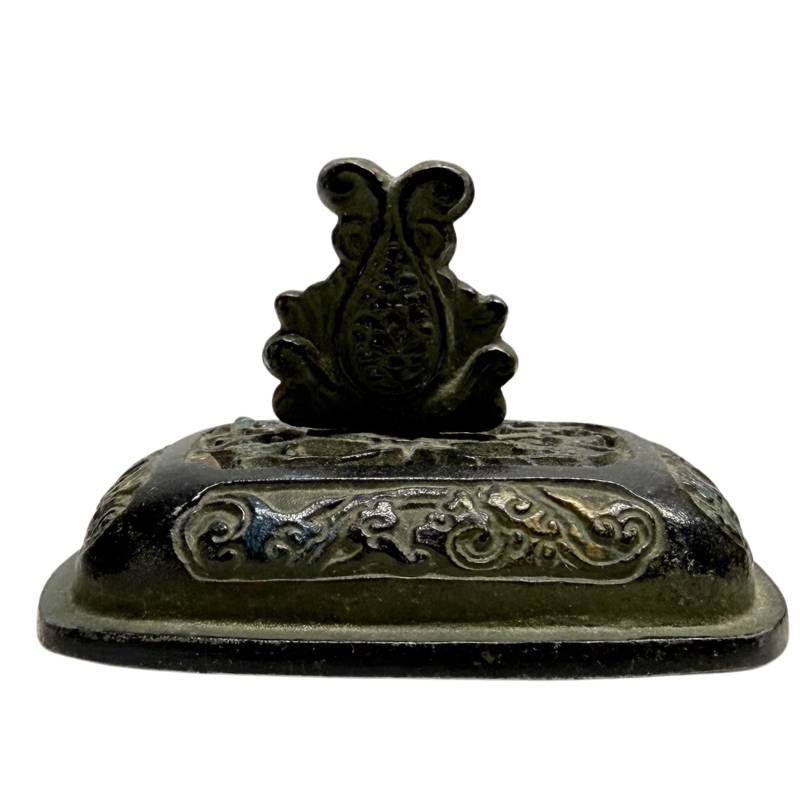 Detailopname van het losse bronzen deksel met wolkenreliëf, sporen van goud en een centrale knop in de vorm van een lotusjuweel.
