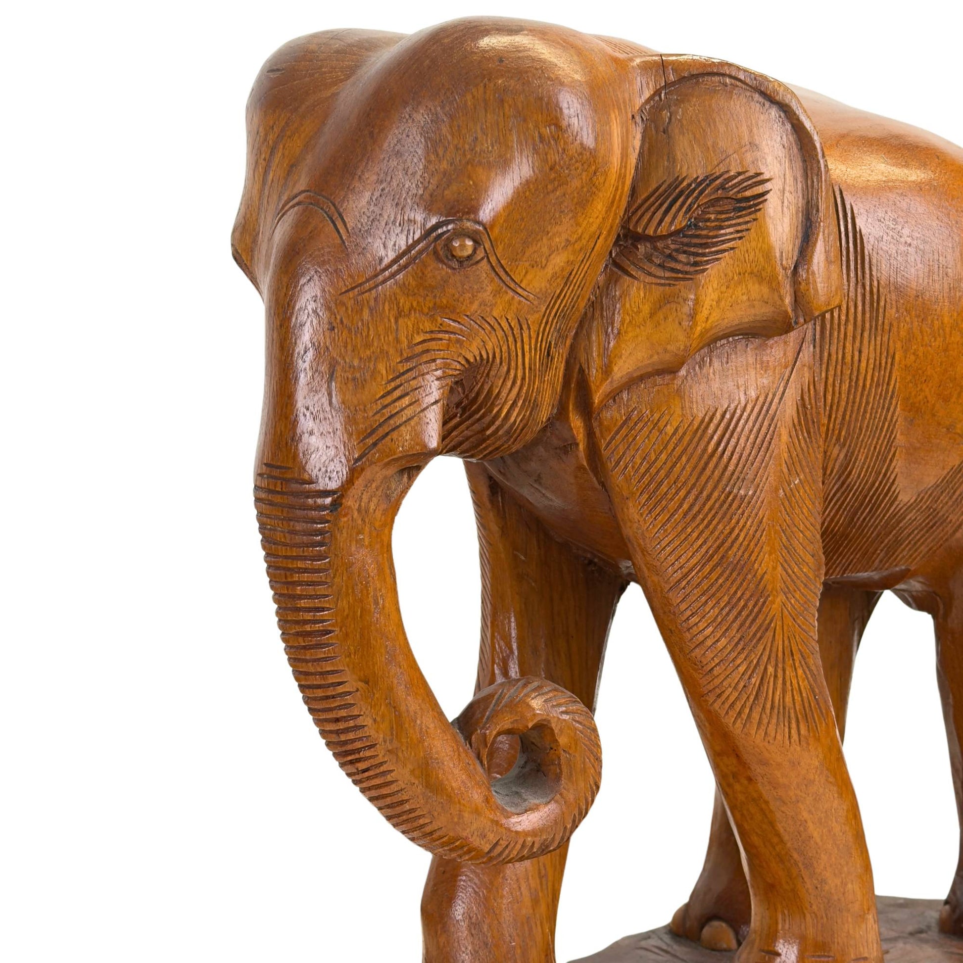Sfeervolle close-up van de kop van de kleinste teakhouten olifant met de spiraalvormig opgerolde slurf en de verfijnd uitgesneden details rond het oog en de oren.