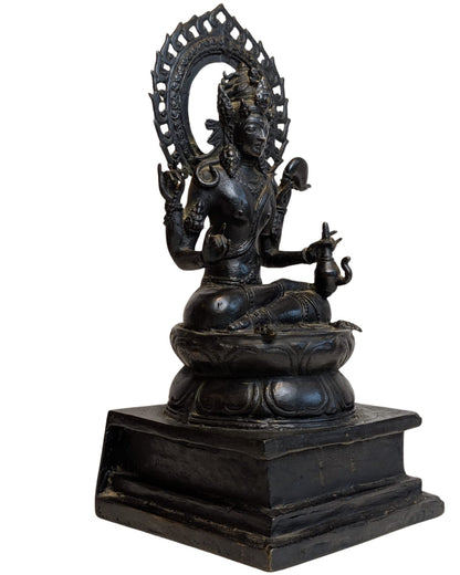Right three-quarter view of seated bronze Vishnu with four arms, lotus base and openwork aureole