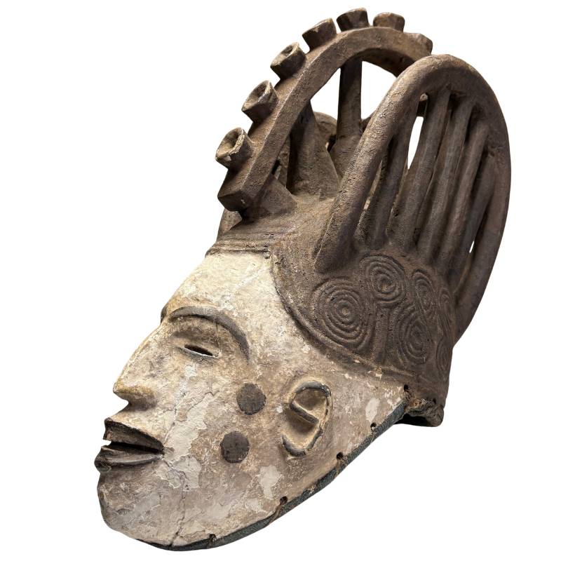 Oud Afrikaans masker met witte patina, handgesneden ritueel object met donkere hoofdtooi en spiraalornamenten