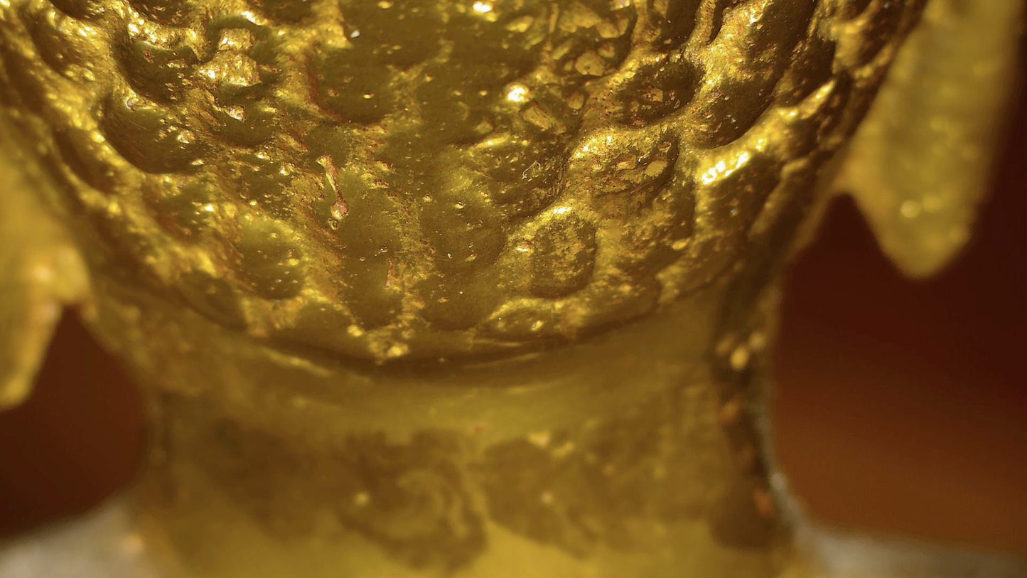 Microscopic detail of old gilding remnants and layered patina on the Tibetan Buddha