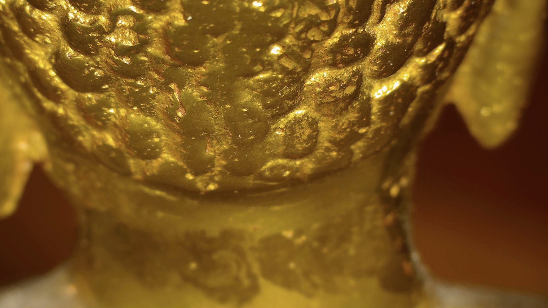 Microscopic detail of old gilding remnants and layered patina on the Tibetan Buddha